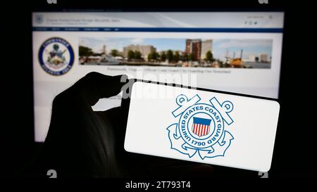 Personne tenant un téléphone portable avec le sceau de la Garde côtière des États-Unis (USCG) devant la page Web. Concentrez-vous sur l'affichage du téléphone. Banque D'Images