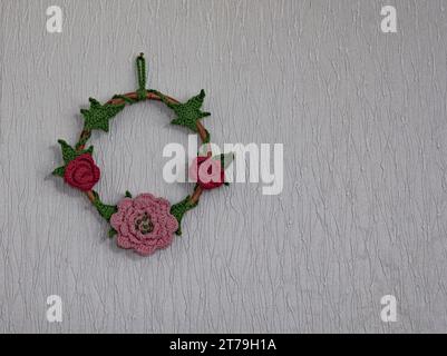 Bague en bois avec des fleurs au crochet et des feuilles en rouge, rose et vert sur fond blanc Banque D'Images