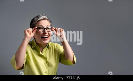 surprise femme âgée des années 50 regardant à travers des lunettes sur les ventes de vendredi vert sur fond gris avec espace de copie Banque D'Images