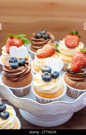 Cupcakes au chocolat et à la vanille avec des myrtilles et des fraises fraîches sur un support à gâteaux en marbre Banque D'Images