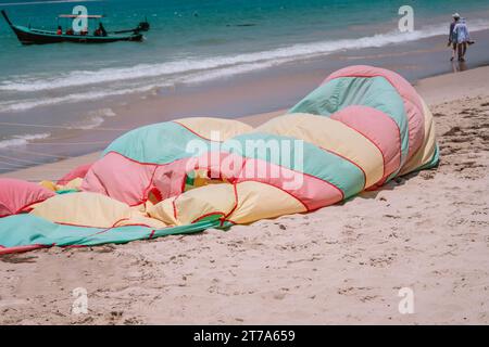 Parachute coloré dégonflé repose sur la plage de sable près de la ligne de bord de mer après le vol.Close up photo Banque D'Images