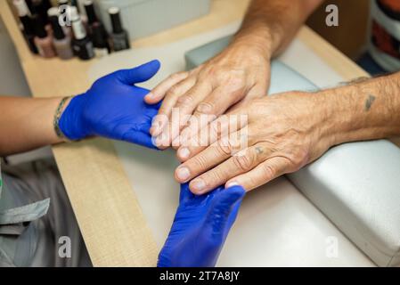 Manucure pour hommes. Les mains d'un homme âgé sont tenues par un spécialiste de manucure dans un salon de beauté. Vue d'en haut Banque D'Images