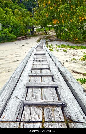 Un chemin en bois abîmé et fissuré qui traverse le sable. Ancienne rampe en bois dans les dunes Banque D'Images