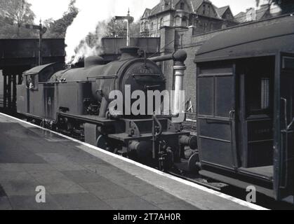 Années 1950, historique, une locomotive à vapeur de l'époque, 67788, sur un quai d'une gare, Angleterre, Royaume-Uni. Le wagon de chemin de fer en face a le mot Garde écrit sur la porte. Construite par Robert Stephenson & Hawthorn, la locomotive LNER L1 Class est entrée en service en 1950 au dépôt de Neasden, à Londres. Elle a été retirée en 1962. Banque D'Images