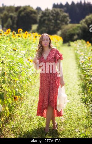 Jeune femme à la mode avec chapeau à la main, debout dans un champ de tournesols Banque D'Images