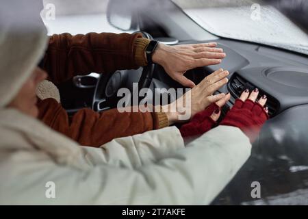 Mains de jeune couple en vêtements d'hiver assis devant le poêle à l'intérieur de la voiture pendant le voyage et gardant leurs mains contre l'air chaud Banque D'Images