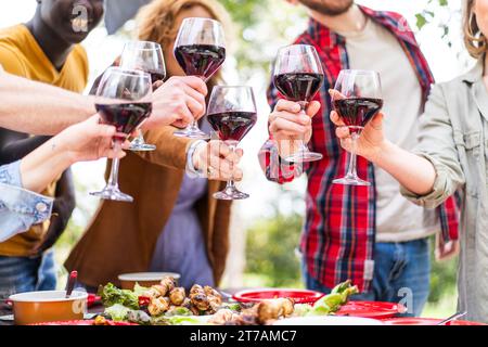 Un groupe d'amis grimpant avec des verres à vin rouge lors d'un rassemblement en plein air, symbolisant la célébration et la connexion sociale. Banque D'Images