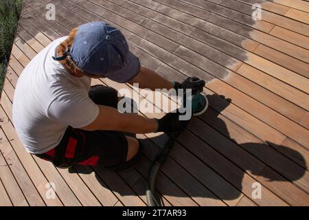 Homme ponçant et nettoyant le pont en bois avec la ponceuse électrique Banque D'Images