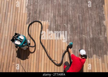 Vue de dessus de la réparation de terrasse en bois, entretien des planches de terrasse gris ipe, ponçage manuel avec ponceuse électrique orbitale connectée au collecteur de poussière Banque D'Images