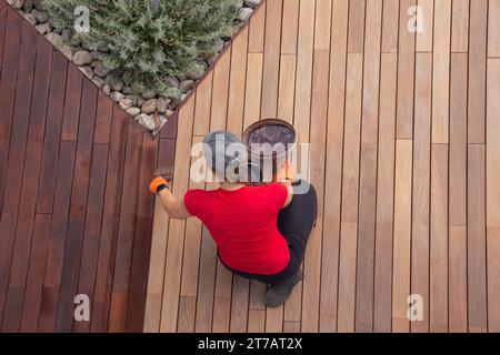 Femme travailleuse peignant le pont en bois avec la vue de dessus de seau d'huile de pont de protection Banque D'Images