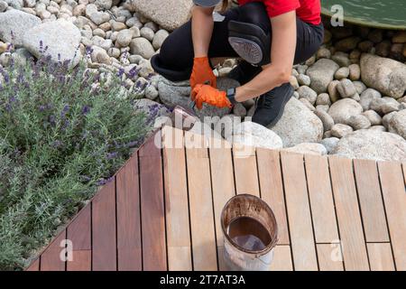 Application d'huile de terrasse en bois par brosse, tâche d'entretien extérieur de la maison pour le printemps. Personne appliquant le traitement de protection sur la surface en bois en gros plan Banque D'Images