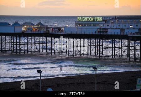 Brighton UK 14 novembre 2023 - Un nageur se dirige vers la mer par Brighton Palace Pier après une journée de soleil et d'averses le long de la côte sud : Credit Simon Dack / Alamy Live News Banque D'Images