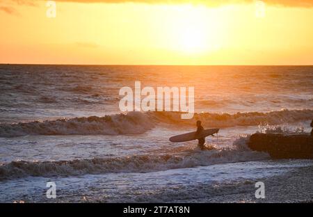 Brighton UK 14 novembre 2023 - Un surfeur entre dans la mer à Brighton au coucher du soleil après une journée de soleil et d'averses le long de la côte sud : Credit Simon Dack / Alamy Live News Banque D'Images