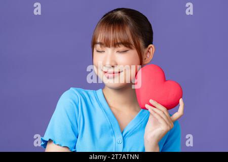 Belle femme tient le cœur rouge, isolé sur fond violet Banque D'Images