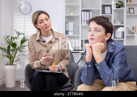 Adolescent pensif à un rendez-vous avec une psychologue féminine, assis dans un bureau moderne, immergé dans ses pensées, consultant un psychothérapeute, problèmes d'intimidation chez les adolescents à l'école. Banque D'Images