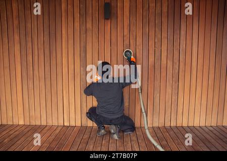 Homme de travail ponçant le parement en bois ipe avec ponceuse orbitale, entretien de plate-forme en bois Banque D'Images