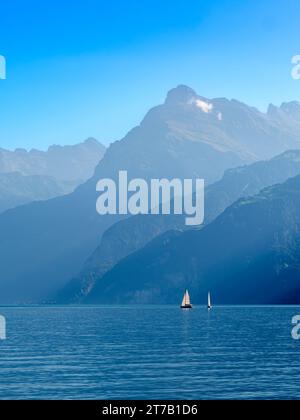 Contours des montagnes par le lac suisse Urnersee dans la lumière brumeuse de jour. Voiliers sur le lac Banque D'Images