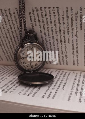 Une montre de poche antique est affichée sur le dessus d'un livre ouvert sur une table, offrant une esthétique intemporelle Banque D'Images