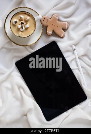 Une tablette se trouve sur un fond blanc à côté d'une tasse de café fumante, suggérant un moment de détente et de contemplation Banque D'Images