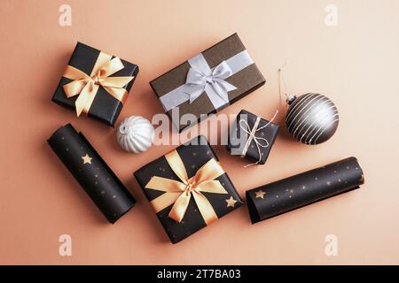 Cadeaux de Noël dans des boîtes noires avec des noeuds dorés et argentés sur fond beige. Vue de dessus, pose à plat. Banque D'Images