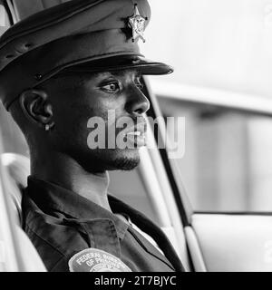 Portrait de rue noir et blanc d'un jeune officier de prison attendant dans sa voiture de patrouille Banque D'Images