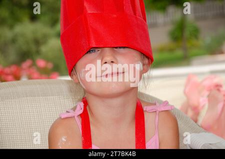 Une fille blanche de 5 ans dans un chapeau de chef rouge et un tablier. Gros plan de son visage taché de farine. Elle a les yeux bleus. Banque D'Images