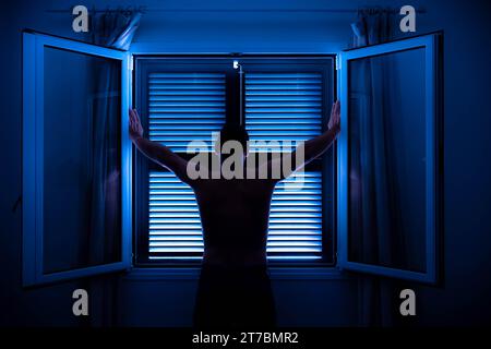 homme méconnaissable face vers le haut avec les bras levés devant la fenêtre Banque D'Images