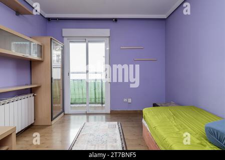 Un petit salon dans une maison avec des meubles en bois clair, parquet, accès à une terrasse avec des portes en aluminium blanc et en verre et peintes violettes Banque D'Images