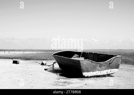 Une image fine art en noir et blanc d'un vieux bateau de pêche en bois sur le sec à marée basse dans le sud sauvage de l'île Maurice. Banque D'Images