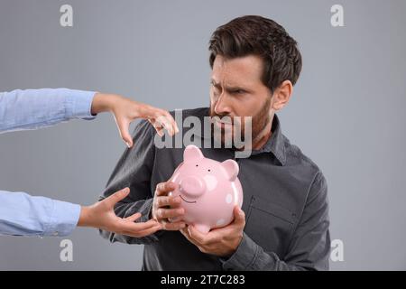 Homme essayant de protéger la tirelire de la femme sur fond gris clair. Soyez prudent - fraude Banque D'Images