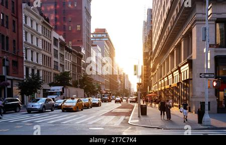 Intersection animée avec des gens, des taxis et des voitures à l'angle de la 5e Avenue et de la 23e rue à Manhattan, New York City avec lumière du soleil sur le backgr Banque D'Images