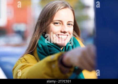 Jeune femme charge avec câble de recharge pour voiture électrique dans la ville Banque D'Images