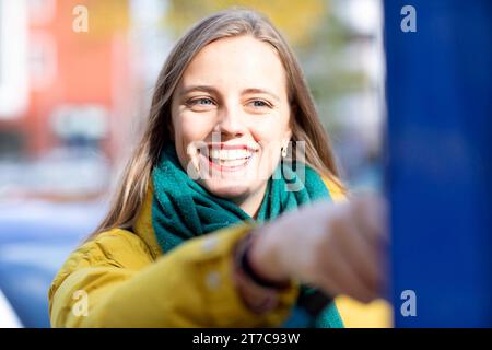 Jeune femme charge avec câble de recharge pour voiture électrique dans la ville Banque D'Images