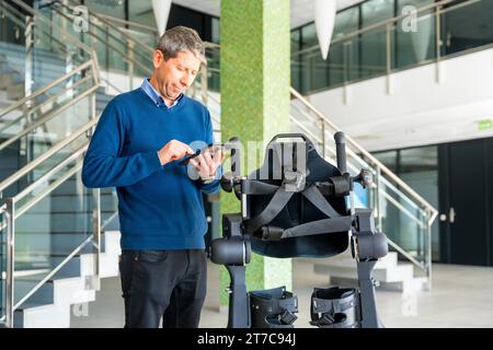 Ingénieur informatique en exosquelette mécanique regardant le robot avec une tablette. Physiothérapie dans un hôpital moderne : squelette robotique. Physiothérapie Banque D'Images