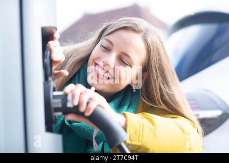 Jeune femme charge avec câble de recharge pour voiture électrique dans la ville Banque D'Images