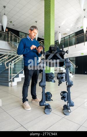 Ingénieur informatique en exosquelette mécanique regardant le robot avec une tablette. Physiothérapie dans un hôpital moderne : squelette robotique. Physiothérapie Banque D'Images