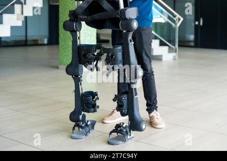 Ingénieur informatique méconnaissable en exosquelette mécanique regardant le robot avec une tablette. Physiothérapie dans un hôpital moderne : squelette robotique. Banque D'Images