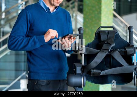 Ingénieur informatique méconnaissable en exosquelette mécanique regardant le robot avec une tablette. Physiothérapie dans un hôpital moderne : squelette robotique. Banque D'Images