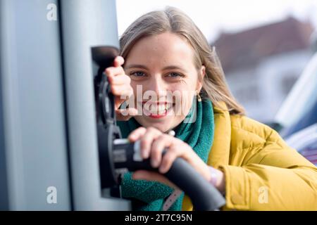 Jeune femme charge avec câble de recharge pour voiture électrique dans la ville Banque D'Images