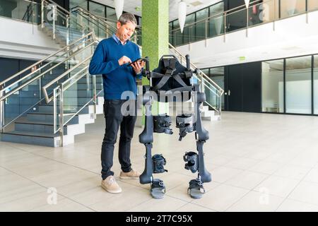 Ingénieur informatique en exosquelette mécanique regardant le robot avec une tablette. Physiothérapie dans un hôpital moderne : squelette robotique. Physiothérapie Banque D'Images