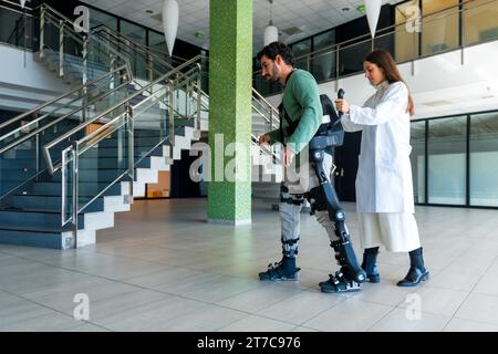 Exosquelette mécanique, physiothérapeute médecin femme marchant avec une personne handicapée aidée par un squelette robotique, physiothérapie dans un hôpital moderne Banque D'Images