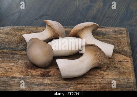 Champignons d'huîtres royales frais, varient en tailles, reposent sur une planche à découper en bois, fond gris-bleu surface en bois teinté, scène vibrante de préparations alimentaires Banque D'Images