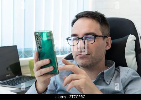 un jeune homme souriant lit des informations sur un smartphone. Jeune homme d'affaires confiant utilisant le phon cellulaire Banque D'Images