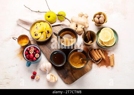 Tasses de thé aux épices au curcuma sain avec des ingrédients : citron, gingembre, bâtons de cannelle et miel sur fond blanc, vue de dessus. Remède stimulant le système immunitaire. Banque D'Images