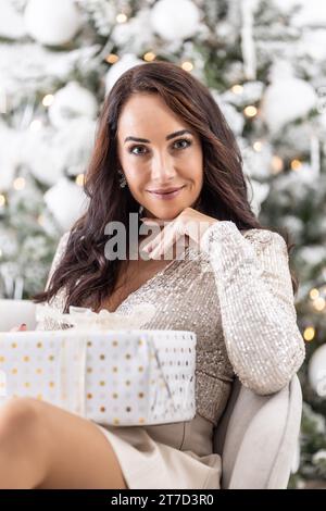 Jolie brune attend pour Noël assis devant l'arbre avec un cadeau de Noël en boîte sur ses genoux. Banque D'Images