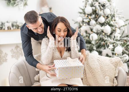 Femme excitée découvre que son homme a mis un cadeau de Noël devant elle. Banque D'Images
