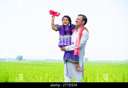 Plan large d'enfant fille de village heureux jouant avec jouet d'avion tandis que le père tenant ou portant près de terres agricoles - concept de relation, parental Banque D'Images