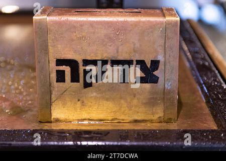 Une tzedakah en métal doré (un mot hébreu qui signifie «charité») boîte de collecte assise sur une table à Jérusalem dehors sous la pluie. Banque D'Images