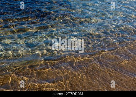 Aquamarine et vagues jaunes au-dessus des rivulettes texturées de sable sur le rivage de la côte méditerranéenne en Israël. Banque D'Images