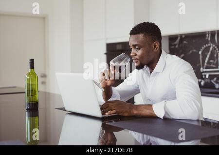 Homme d'affaires solitaire noir africain se sent fatigué épuisé assis assis travaillant en ligne amd boire du vin seul à la maison Banque D'Images